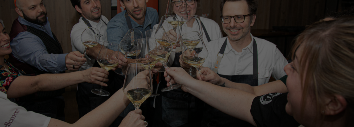 A group of chefs cheers'ing each other over a glass of white wine.